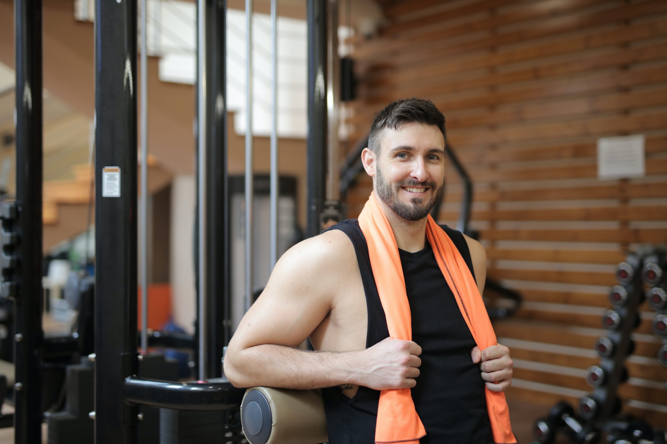 There are many fascinating facts about men's health, especially in relation to cardiovascular disease. In this image, a man at the gym is smiling at the camera while holding a towel behind his neck.
